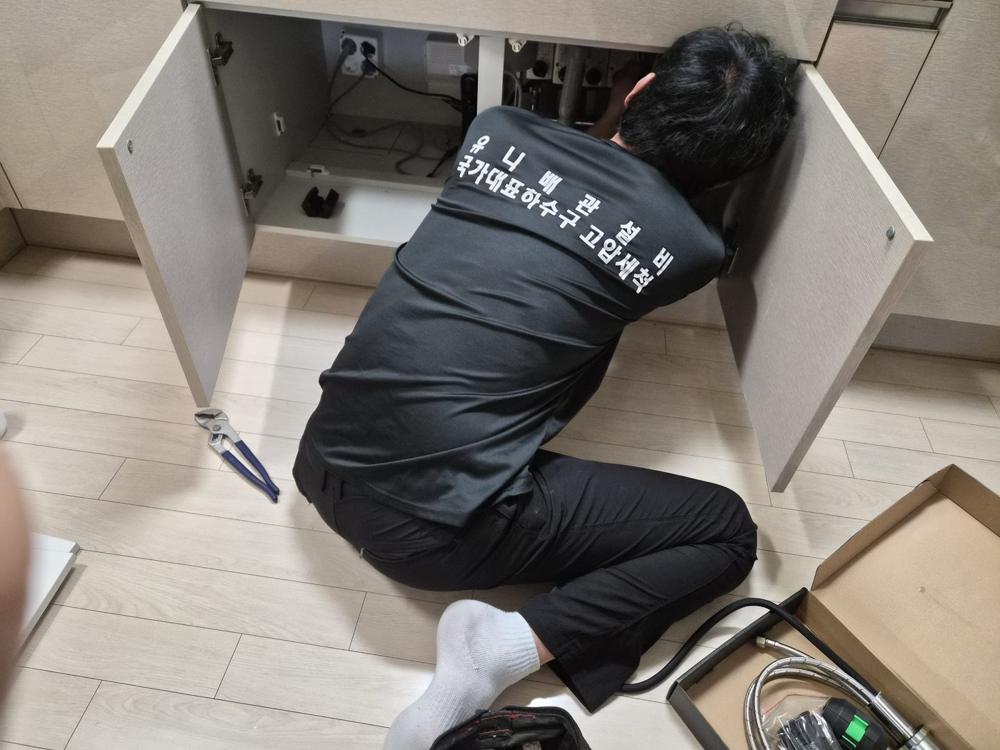 싱크대 하부장 안쪽에서 배관을 확인하는 작업자
